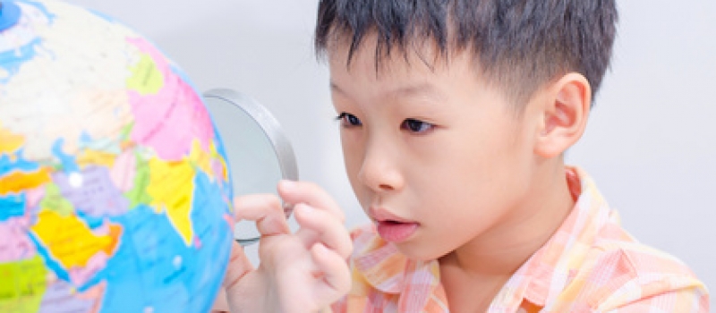 Asian boy looking at a globe by magnifying glass